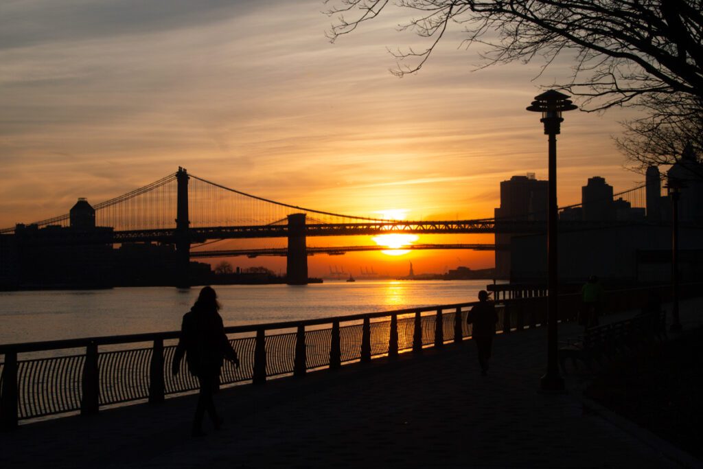 East River Park, Manhattan Lower East Side, view of Manhattan and Brooklyn Bridges and Statue of Liberty at sunset.