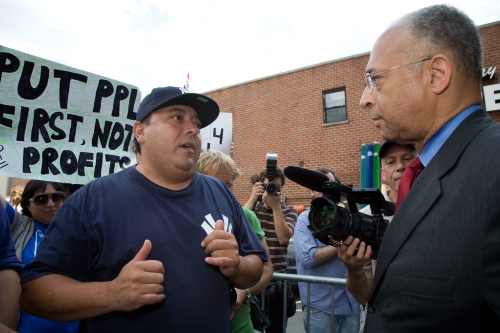 After a press conference outside the Stella D’oro factory, longtime employee Eddie Marrero (left) urges NYC Comptroller and mayoral candidate William Thompson Jr. (right) to follow through on his promise to help the workers. "Stella D'oro Workers Fight for Jobs," from The Clarion (Professional Staff Congress, City University of New York).