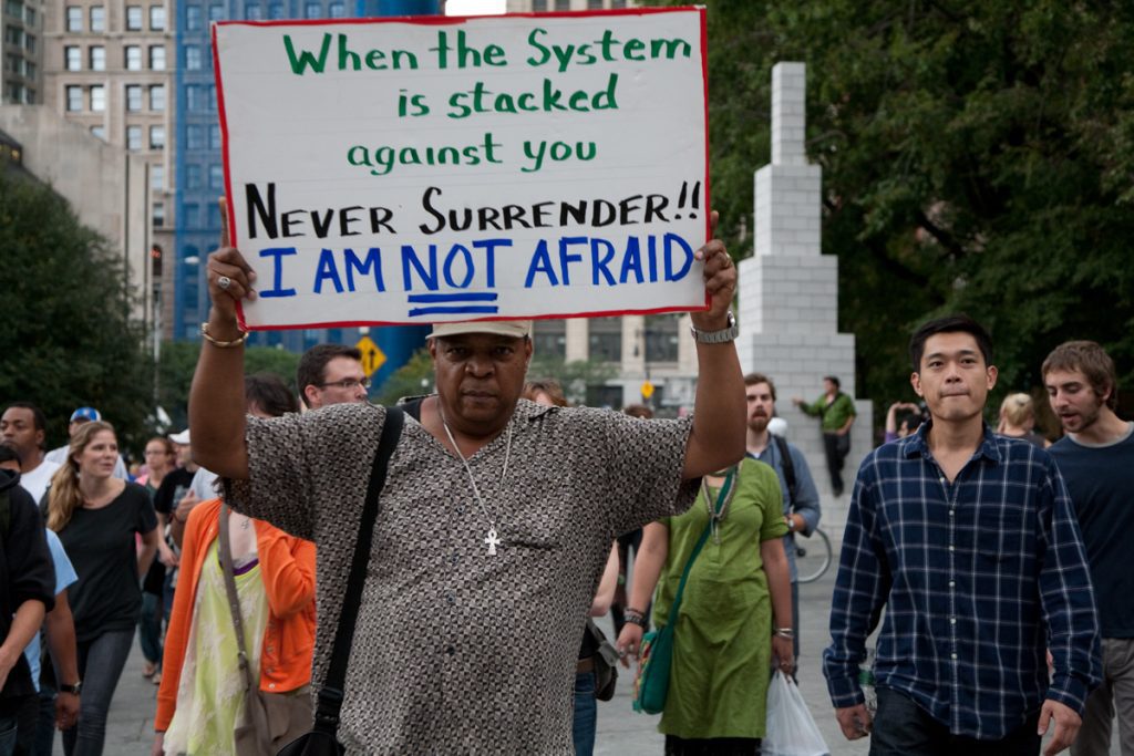 Occupy Wall Street protester with sign, "When the system is stacked against you, never surrender. I am not afraid."
