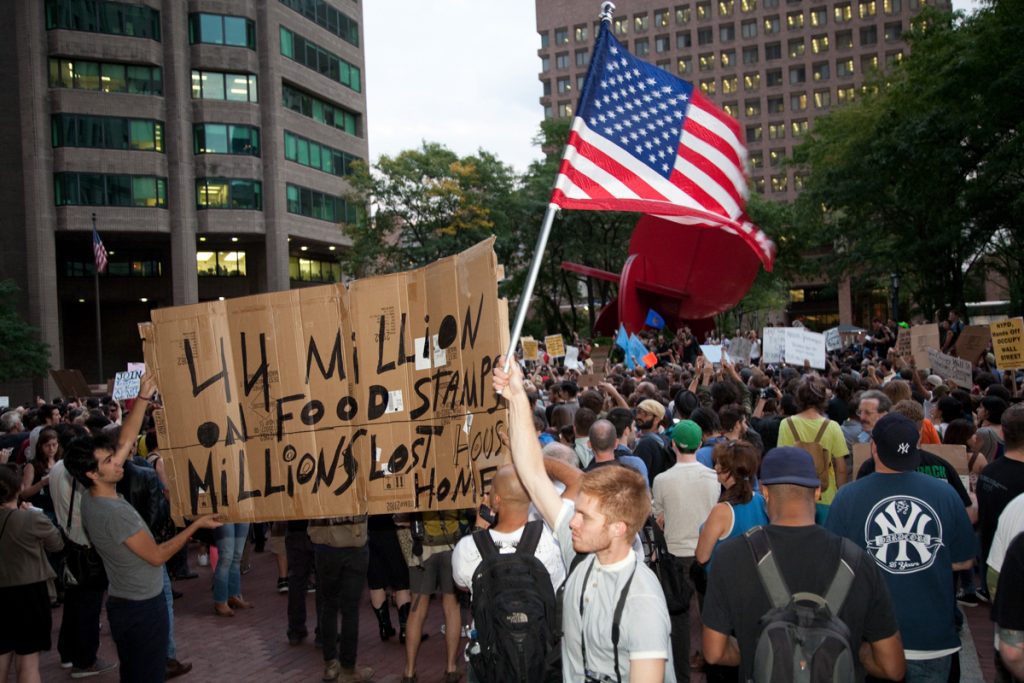 "44 million on food stamps, millions lost homes" sign and American flag at 1 Police Plaza protest